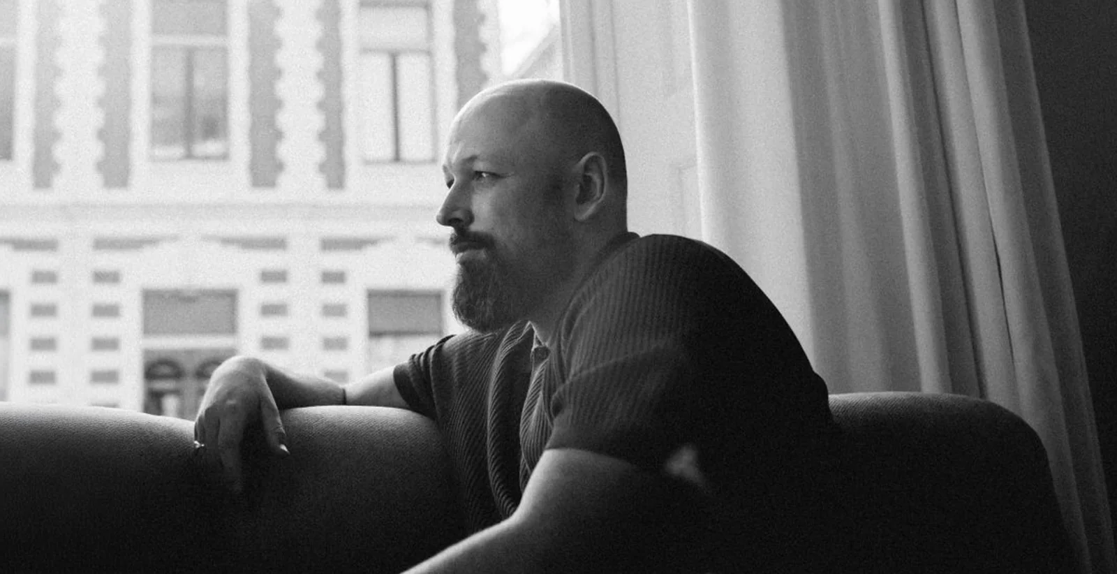 Alex van Binsbergen, seated by a tall window.